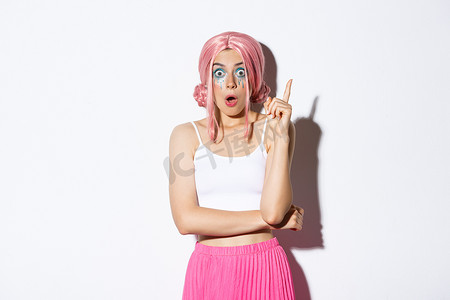 戴着粉色派对假发、化着亮妆的创意女性形象，提出想法，在尤里卡标志上举起食指，站在白色背景上