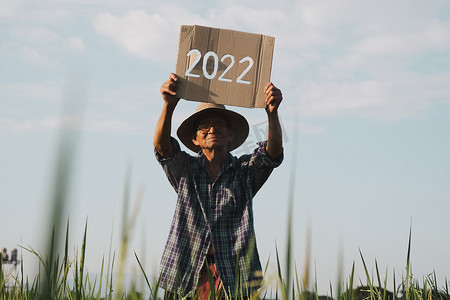 夕阳下，一位老农民站在稻田里，举着 2022 年新年标志的剪影。