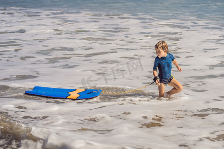 快乐的小男孩在度假时在海滩上玩得开心，带着布吉板