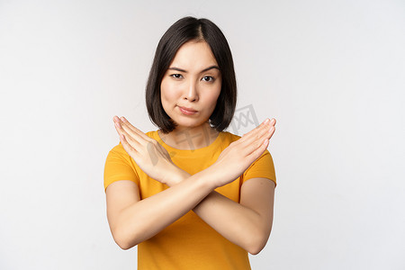 禁止手势摄影照片_亚洲女性的肖像看起来严肃而愤怒，展示停止禁止手势、禁忌标志、禁止某物、站在白色背景上的黄色 T 恤