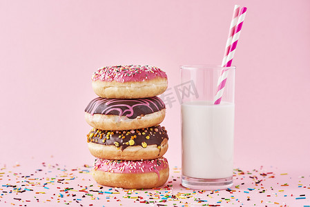 彩色巧克力摄影照片_粉红色背景上装饰着一叠彩色甜甜圈和一杯牛奶