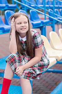 蓝色校服摄影照片_穿着校服的漂亮女孩在学校体育场的蓝色和黄色论坛上。