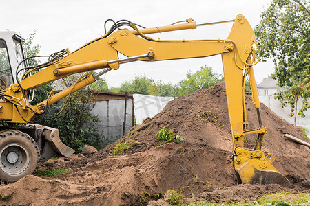 液压活塞和斗式挖掘机在工业场地的一堆沙子旁边挖掘地面