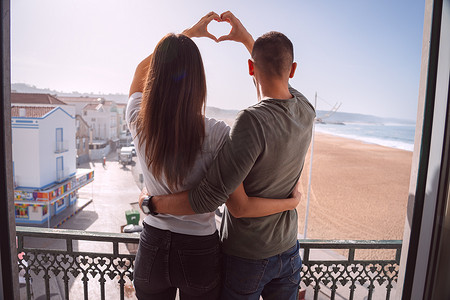 年轻夫妇站在阳台上，用手做心形。