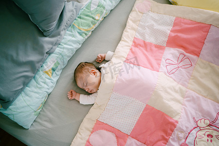 婴儿睡在铺着粉色拼布被子的床上。