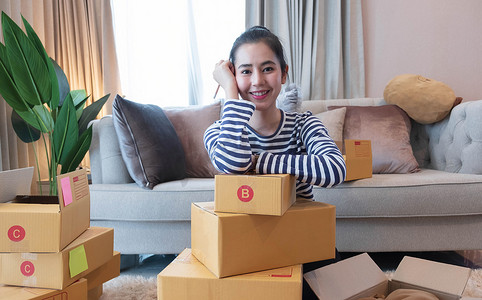 亚洲年轻女性的小型中小企业企业家使用笔记本电脑在家网上购物，在家中用包装盒欢快快乐，自己创业网上创业