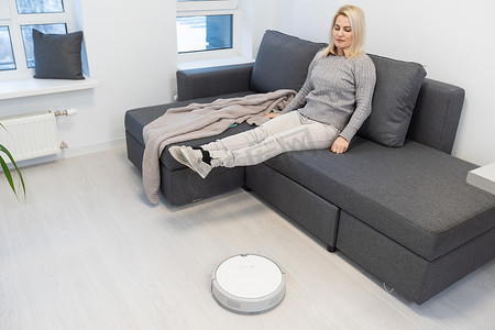 机器人吸尘器清洁房间，而女人则躺在沙发上
