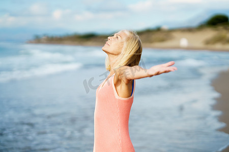 美丽的成熟女人在美丽的海滩张开双臂，享受空闲时间