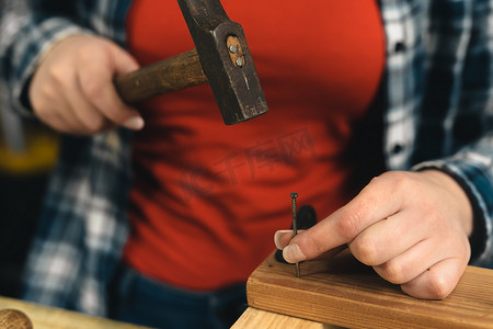 一位年轻女木匠在木板上拿着钉子的手的特写镜头。