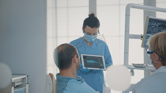 医生患者平板电脑摄影照片_正畸护士在平板电脑上拿着 X 射线结果向患者展示