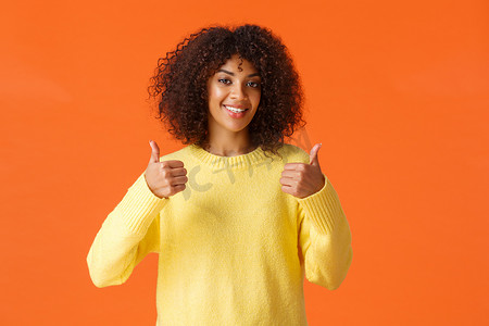 腰上拍摄可爱的支持性非洲裔美国女性对好主意感到高兴，竖起大拇指和微笑，同意你的观点，给出积极的答案，推荐产品，橙色背景