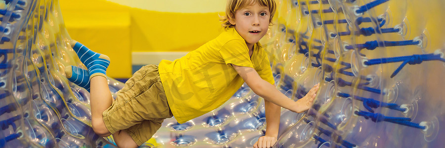 长摄影照片_可爱的小男孩，在 Zorb 中玩耍，中间有一个孔的滚动塑料圆筒环，室内横幅，长格式