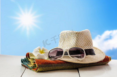 大气时尚背景摄影照片_帽子、眼镜、围巾、鲜花放在木地板上，以阳光和天空为背景。