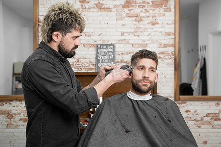 男理发师在理发店用剪刀给男性顾客剪头发。
