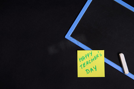 平躺着一张粘贴的黄色便条纸，上面写着教师节快乐，在一块空的空白板上用粉笔写着。