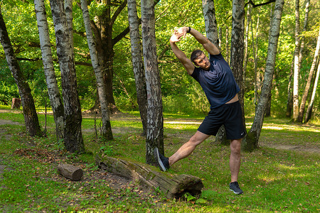 树林摄影照片_一位年轻持久的运动运动员正在户外森林里做伸展运动，周围是森林，橡树。活跃的大自然，锻炼慢跑运动员，树林秋季休闲伸展运动