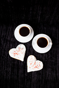 黑色背景上有两杯咖啡和心形饼干