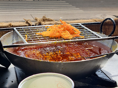 商店的特写镜头，厨师在沸油中油炸许多贾莱比，使其放在金属丝网上，制作街头小吃，这种小吃因其甜味而在印度拉贾斯坦邦斋浦尔流行