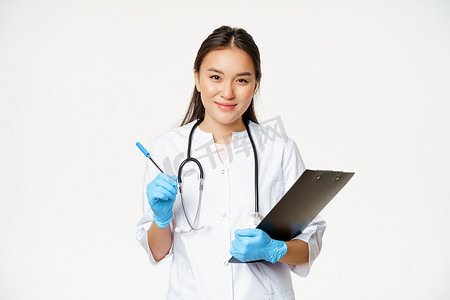 微笑的亚洲医生、女护士拿着剪贴板和笔，穿着带手套的制服，写病人信息，站在白色背景上