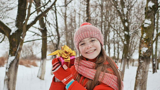 白雪皑皑的森林摄影照片_冬天，一位美丽的年轻女学生站在白雪皑皑的森林里，从朋友手中接过一份快乐的礼物。