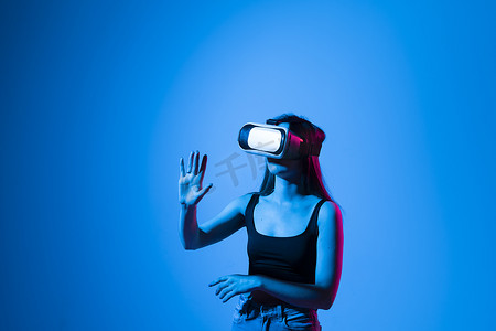 年轻女子的特写镜头站在工作室里，戴着 VR 眼镜，用手在虚拟空间中滑动滚动缩放，同时与虚拟宇宙中的物体进行交互。