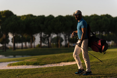 高尔夫球手在美丽的日落时行走并携带高尔夫球包