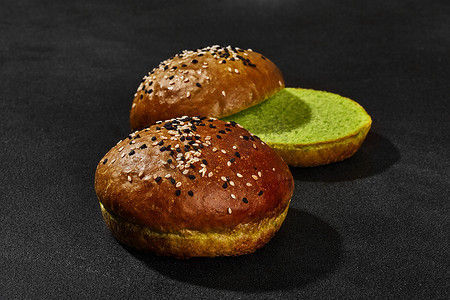 新鲜、美味的烤绿色面包，撒上深色和白色芝麻，黑色背景，有复制空间。