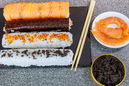 不同类型的寿司卷，配有美味的黑鱼子酱配料和黑盘上的筷子。