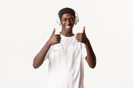听歌学生摄影照片_满意、微笑的非洲裔美国人的肖像，享受着美妙的音乐，竖起大拇指表示赞同，戴着耳机听歌