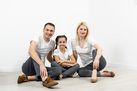 幸福的家庭父亲母亲和孩子们坐在空荡荡的白墙上的地板上