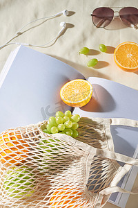 阳光葡萄摄影照片_暑假与水果袋、眼镜、耳机和杂志在浅色背景。