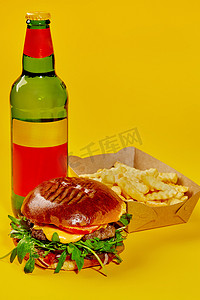 黄色背景中配有小牛肉饼的芝士汉堡、薯条和瓶装饮料