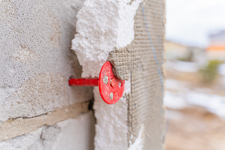 红色销钉的特写将聚苯乙烯泡沫固定在加气混凝土砌块墙上。