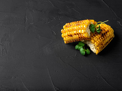 烤黄玉米棒子，黑色背景上有绿豆芽。