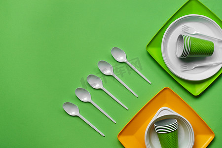 在绿色背景的五颜六色的塑料一次性餐具与复制空间。