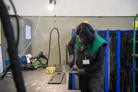 机床摄影照片_一位在现代金属生产和加工行业工作的女性焊接产品并为数控机床做好准备