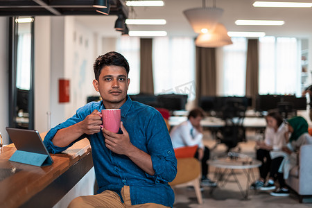 休闲商人在现代开放式创业办公室的休闲区喝茶时使用笔记本电脑从工作中休息