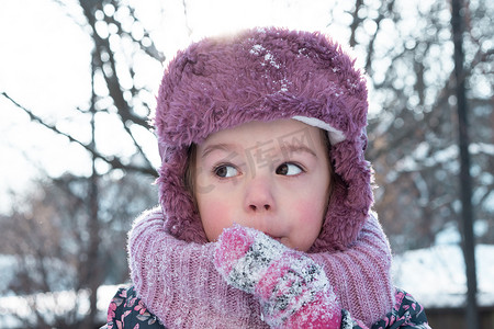 冬天、游戏、家庭、童年概念 — 戴着粉色帽子的正宗学龄前未成年 3-4 岁女孩的特写肖像，在雪天结霜的天气里看着相机摆出微笑。