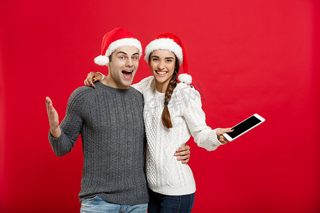 圣诞节概念 — 穿着圣诞毛衣、拿着数字平板电脑的快乐年轻夫妇