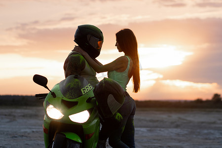 日落时,一对夫妇在海滩上骑着摩托车拥抱