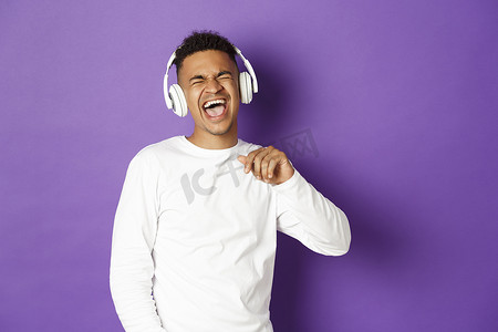 无忧无虑的非洲裔美国人站在紫色背景下跳舞、用无线耳机听音乐、一起唱歌的画面