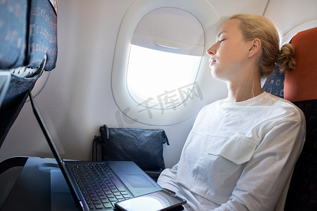 在飞机上睡觉摄影照片_疲惫的女商人在出差期间在飞机上打盹。
