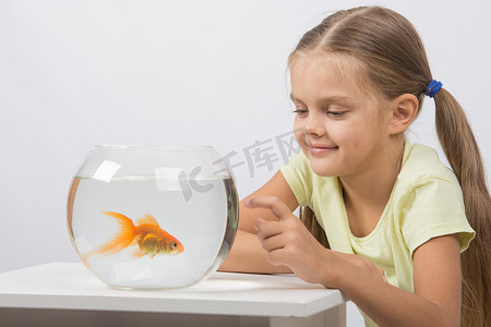 快乐的小女孩用手指敲着金鱼水族馆