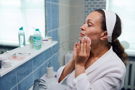 一位美丽的多民族中年妇女在家庭浴室里卸妆，看着镜子的特写肖像
