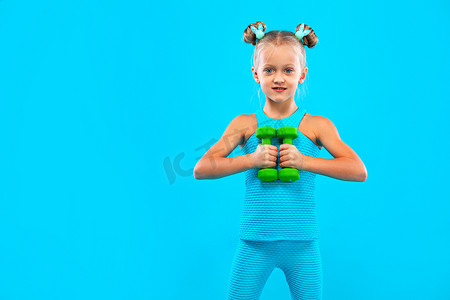 蓝色背景中用哑铃进行健身或瑜伽练习的小女孩