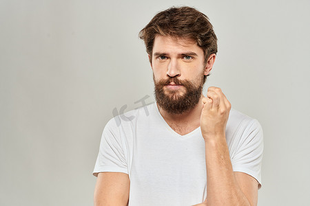 一名身穿白色T恤、留着胡子的男子情绪不悦，面部表情浅色背景