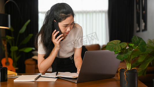商业手机摄影照片_年轻的创业企业家与她的商业伙伴进行电话交谈，在家庭办公室工作