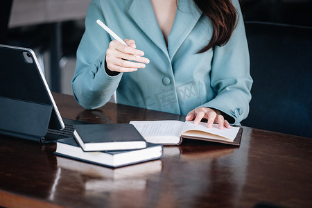 一位女性企业家或女商人在阅读一本制定金融和投资策略的书并在木桌上操作平板电脑时露出微笑。