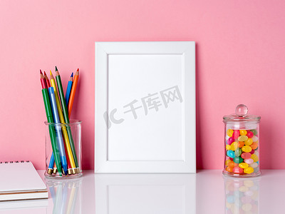 空白的白色框架和罐子里的蜡笔，白色桌子上的糖果，靠在粉红色的墙上，有复制空间