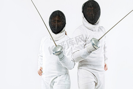两名年轻击剑运动员戴着面具，穿着白色击剑服装，手持剑。